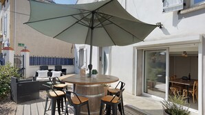 Un'area salotto esterna con un tavolo rotondo in legno, quattro sgabelli da bar e un grande ombrellone.