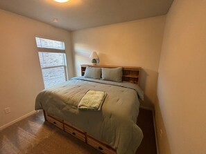 Une chambre à coucher avec un lit, une table de chevet, une lampe, une fenêtre et une porte.