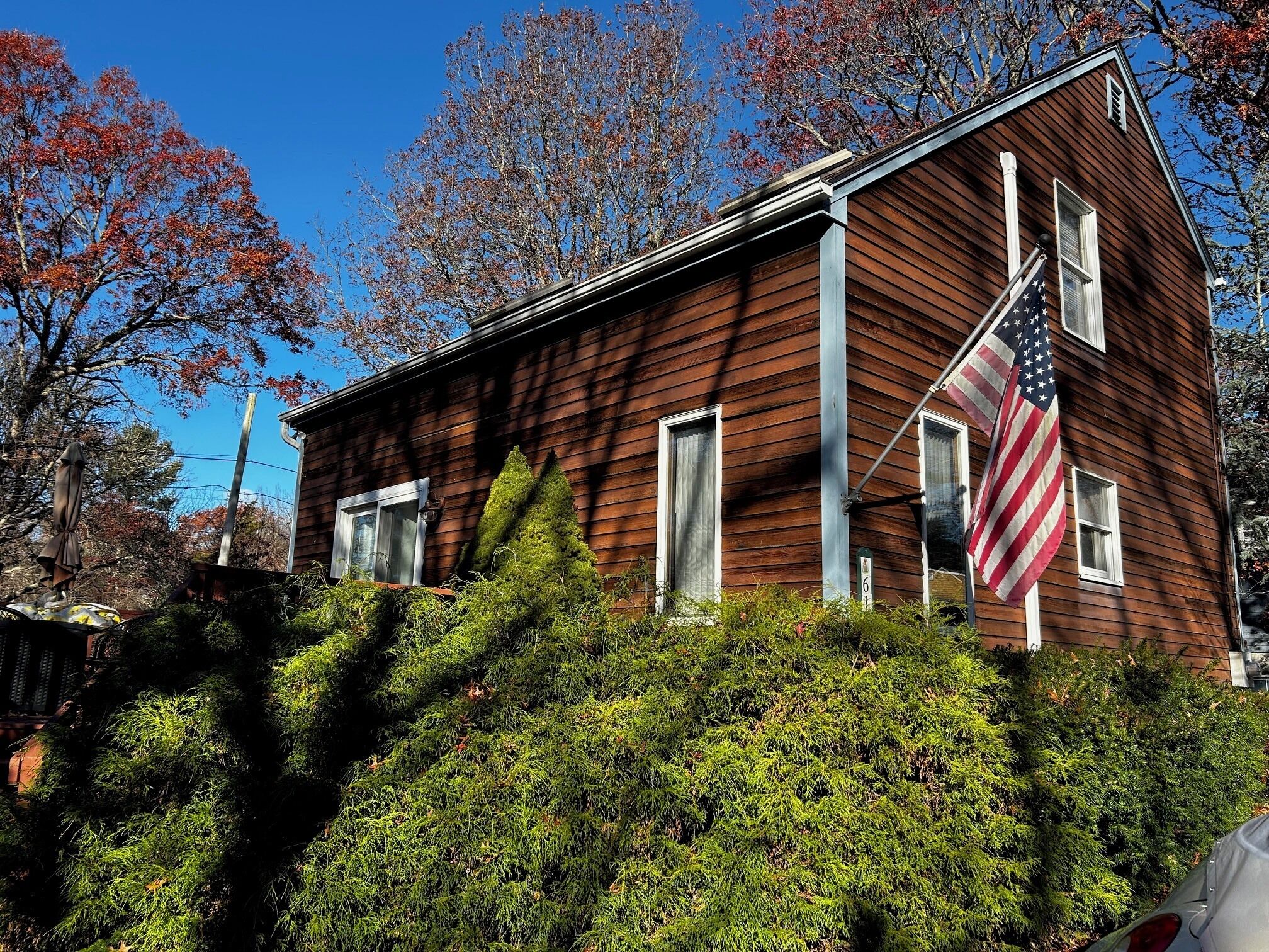 A wooden house with an American flag, surrounded by trees and shrubs.
