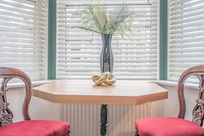 A corner room with a wooden table, two chairs, a potted plant, and white blinds. - Beautifully Designed 1 Bed Flat (Morecambe)