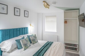 A bedroom with a bed, wall-mounted lights, a radiator, a window with blinds, and a wardrobe.