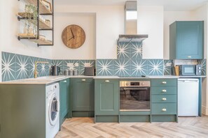A kitchen with a washing machine, a clock, and a stove. - Beautifully Designed 1 Bed Flat (Morecambe)