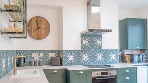 Een moderne keuken met groene kastjes, een marmeren aanrechtblad, een inbouwoven en een wandklok.
