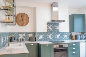 A modern kitchen with green cabinets, a marble countertop, a built-in oven, and a wall-mounted clock. - Beautifully Designed 1 Bed Flat (Morecambe)