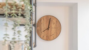 Een houten wandklok met Romeinse cijfers, bevestigd aan een witte muur.