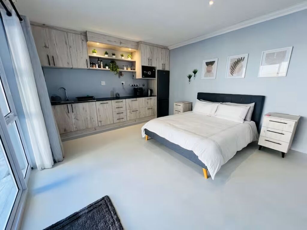 A modern bedroom with a bed, bedside tables, and a small kitchen area.