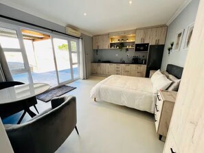 Een moderne slaapkamer met een bed, een bureau en een stoel. Er is een keukenhoek met kasten en apparatuur.