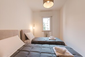 Un dormitorio con dos camas, una ventana y una lámpara.