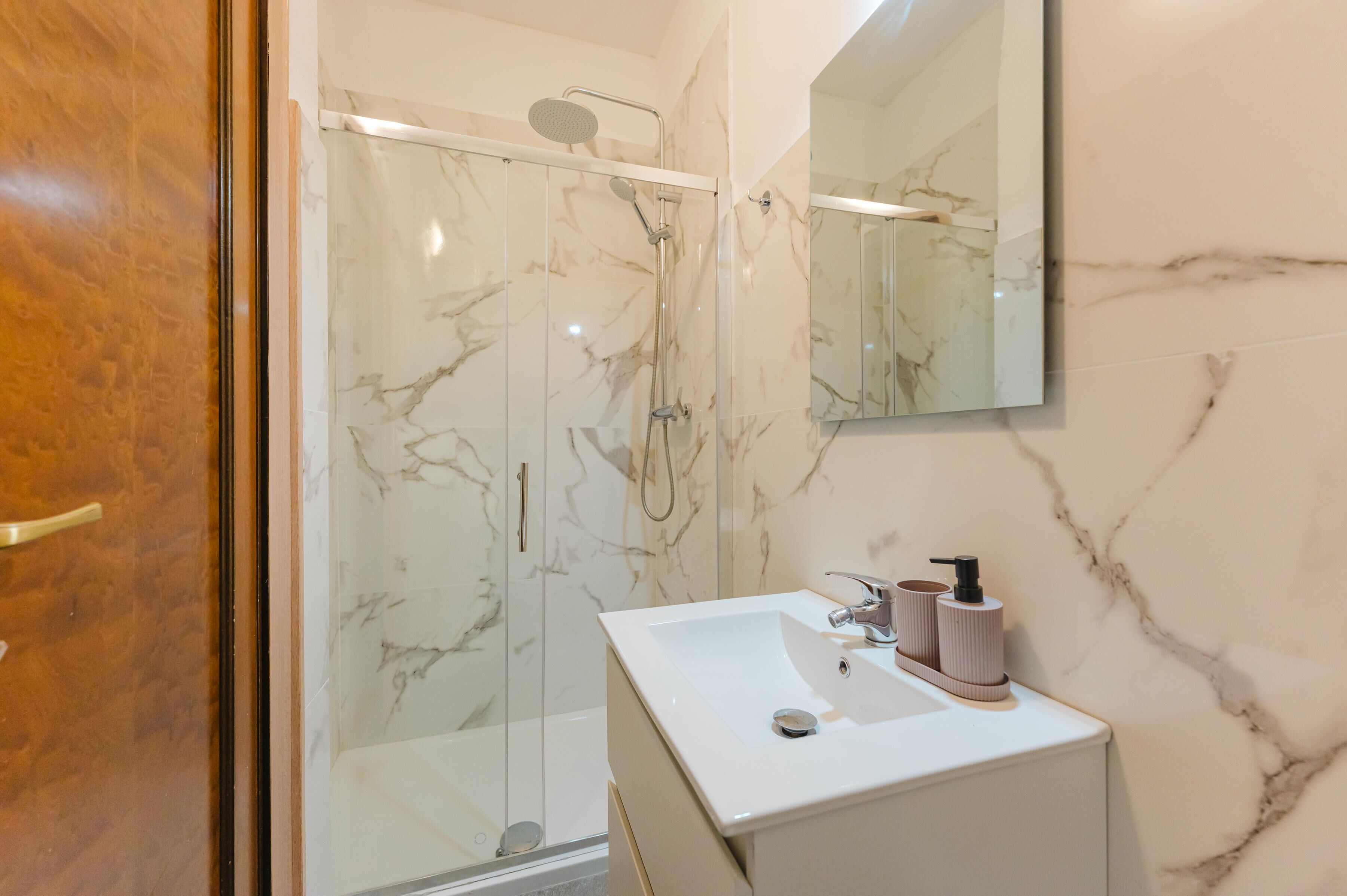 Un baño con ducha de vidrio, un lavamanos blanco y una pared de mármol.