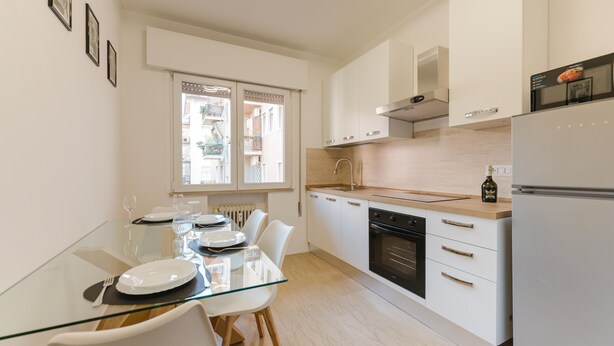 A modern kitchen with white cabinets, a glass dining table, and a built-in oven. - Gaia's Flat - 15 min from Venice (Mestre)