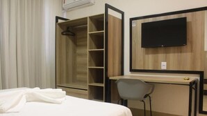 A hotel room with a bed, a desk with a chair, a TV, and a wardrobe. - Hotel Oscar Gold Janaúba (Janaúba)
