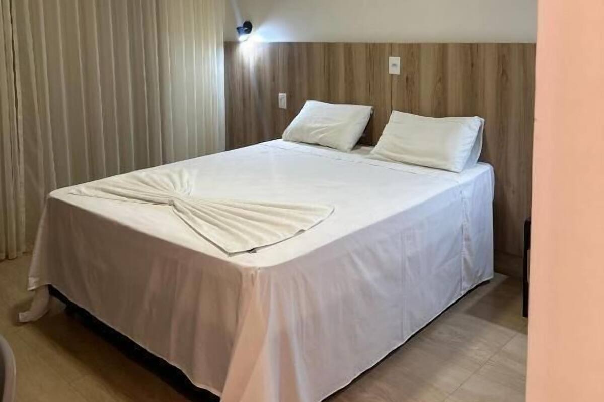 Une chambre d’hôtel avec un grand lit, une tête de lit en bois, un luminaire au plafond et un rideau.