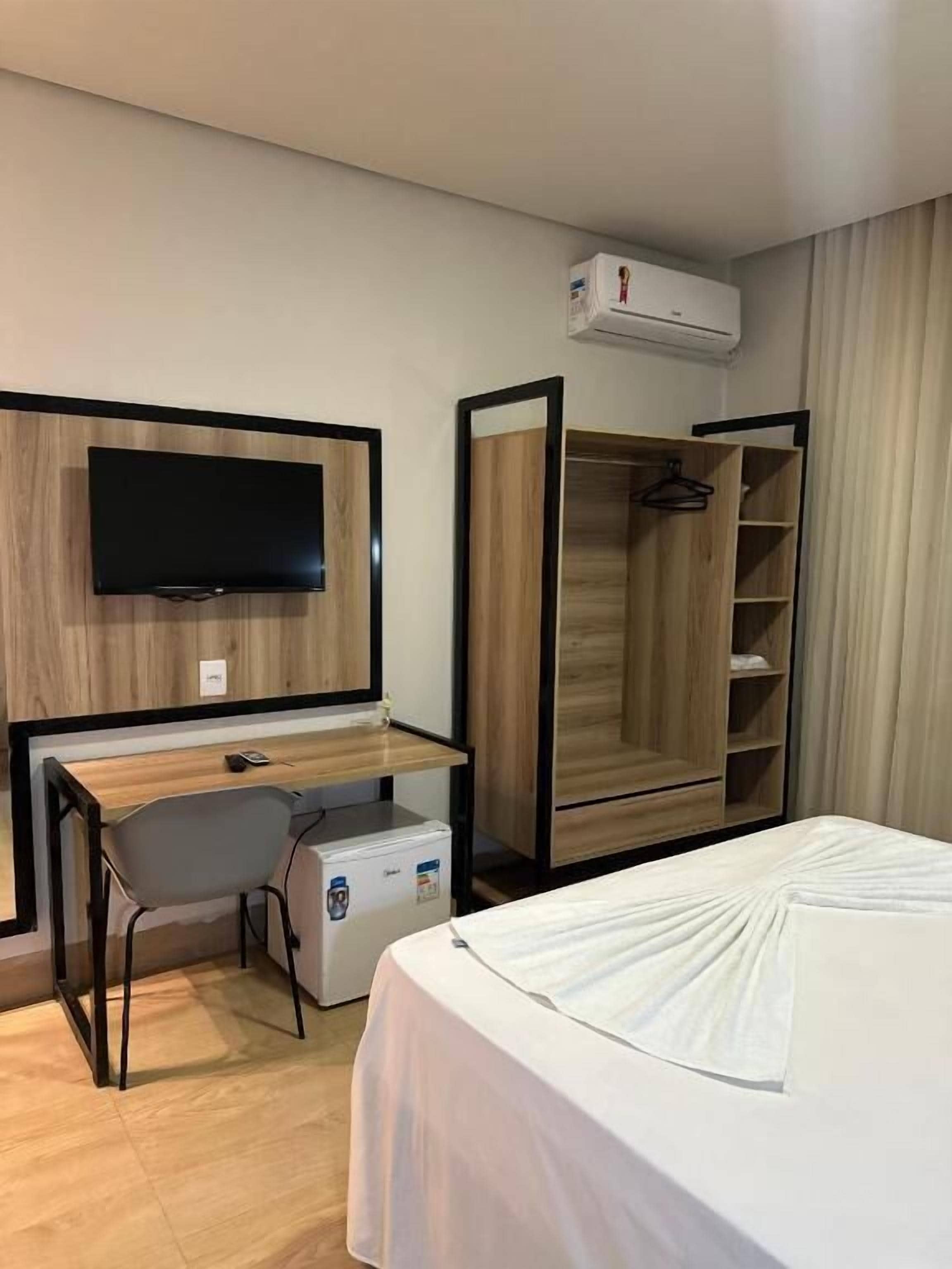 Habitación de hotel con cama, escritorio, silla, televisión, armario y aire acondicionado.