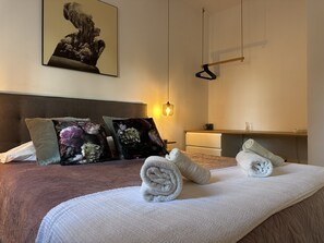 A neatly made bed with rolled towels, a headboard, a bedside table, a hanging light, and a wall-mounted artwork. - Apartamento El Convento - Ole Solutions (Jerez de la Frontera)