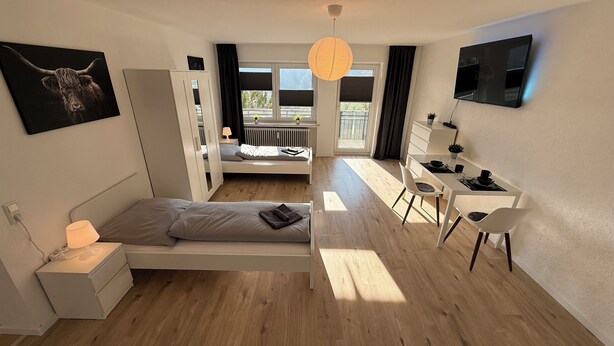 A modern bedroom with a bed, bedside table, lamp, and a desk with chairs. - GNA02.01 - Apartment with 5 beds, modern kitchen, balcony & parking space (Lüdenscheid)