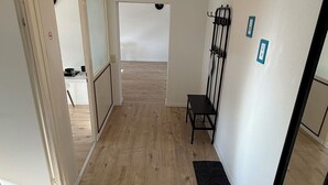 A hallway with wooden flooring, a bench, a wall-mounted rack, and a door leading to another room. - GNA02.01 - Apartment with 5 beds, modern kitchen, balcony & parking space (Lüdenscheid)