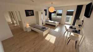 A modern apartment with a bed, a desk, a dining area, and a view of the outdoors. - GNA02.01 - Apartment with 5 beds, modern kitchen, balcony & parking space (Lüdenscheid)