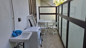 Un petit balcon équipé d’un lave-linge, d’un évier et d’une table avec des chaises.