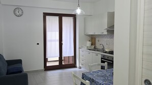 Un espace de vie compact comprenant un canapé, une table à manger, un coin cuisine et une porte donnant sur un espace extérieur.