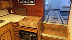 Uma cozinha compacta com um letreiro 'WELCOME', micro-ondas e uma cesta de vime.