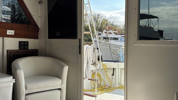 Interior de barco com sofá de couro branco, um banco acolchoado, televisão e vista para o exterior.