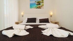 Camera d'albergo con un letto, tende bianche, un quadro che raffigura una costa e due abat-jour.