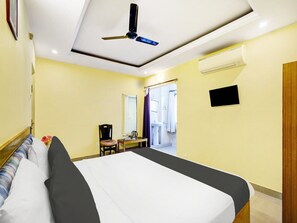 Habitación de hotel con cama, una silla, una mesa con cafetera, espejo y ventilador de techo.