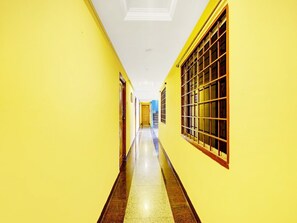 Un pasillo con paredes amarillas y piso de baldosas, que conduce a una habitación con ventana y puerta.