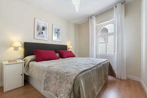 Una camera da letto con un letto, due lampade da comodino, un comodino, una finestra con tende e due quadri appesi al muro.