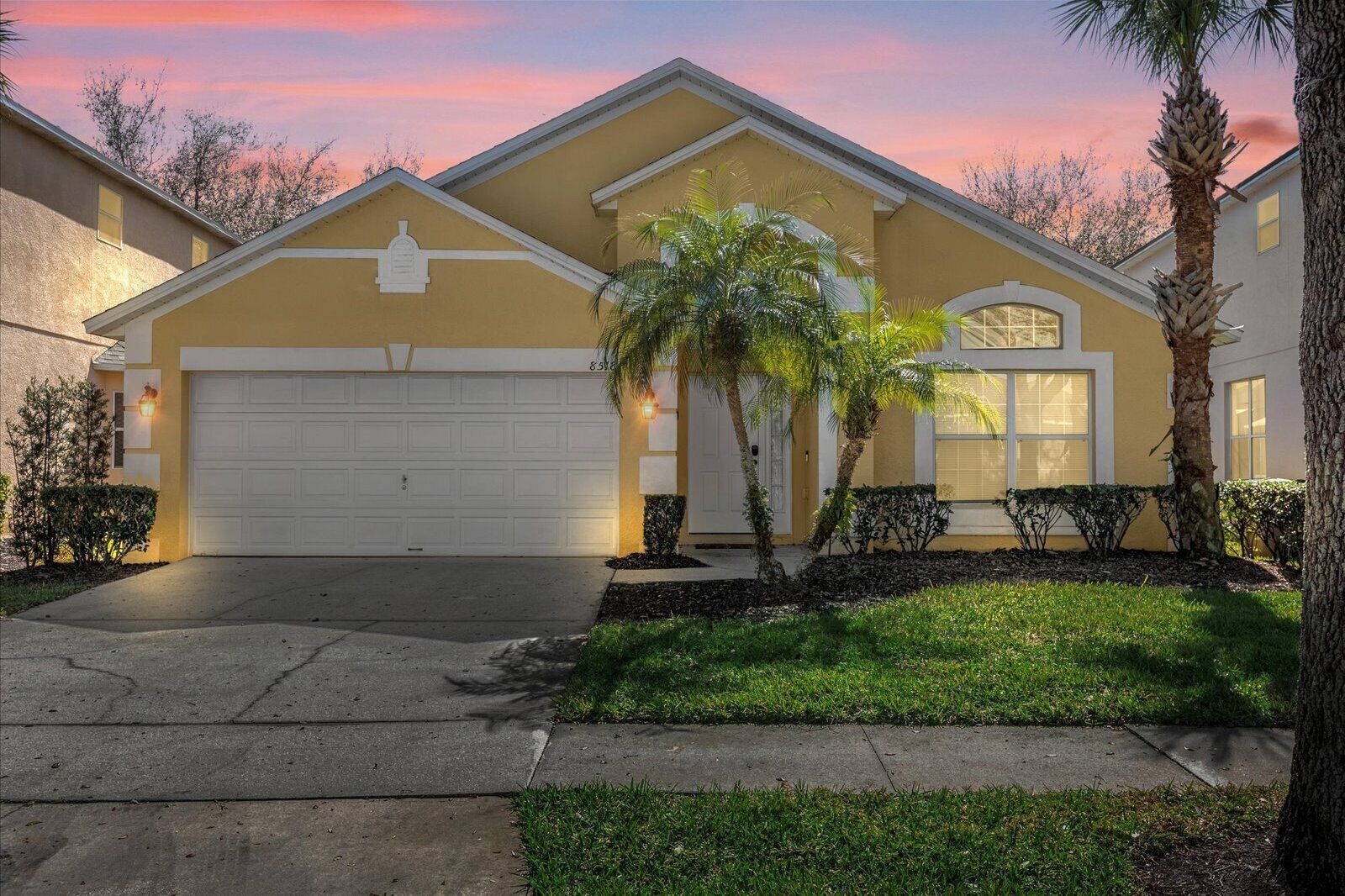 A residential house with a garage, a well-maintained lawn, and a palm tree.