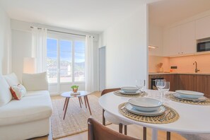 A modern living room with a dining table set for four, a sofa, and a kitchen area with cabinets and a microwave. - 325 L Alba in Cannes (Cannes)