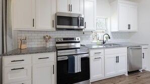 Una cocina con armarios blancos, electrodomésticos de acero inoxidable, encimera de granito y ventana con vistas.