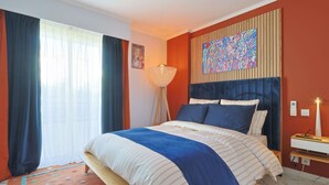 Ein Schlafzimmer mit einem Bett, Vorhängen, einer Lampe, einem Gemälde und einem Nachttisch.