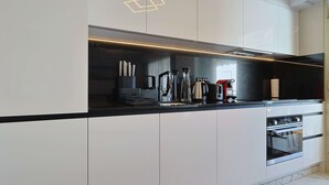 Eine moderne Küche mit weißen Schränken, einer schwarzen Arbeitsplatte und Edelstahlgeräten, darunter ein Backofen und eine Kaffeemaschine.