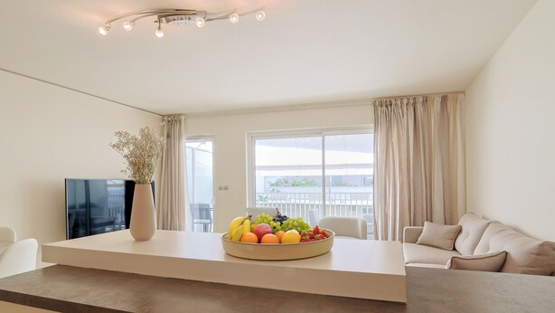 Ein modernes Wohnzimmer mit Flachbildfernseher, Obstschale, Blumenvas und einer Couch.