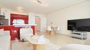 Ein modernes Wohnzimmer mit Flachbildfernseher, einem Essbereich mit Tisch und Stühlen sowie einer Küche mit roten Akzenten.