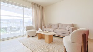 Ein modernes Wohnzimmer mit einer Couch, Sesseln, einem Couchtisch und einer großen Schiebeglastür, die auf einen Außenbalkon führt.