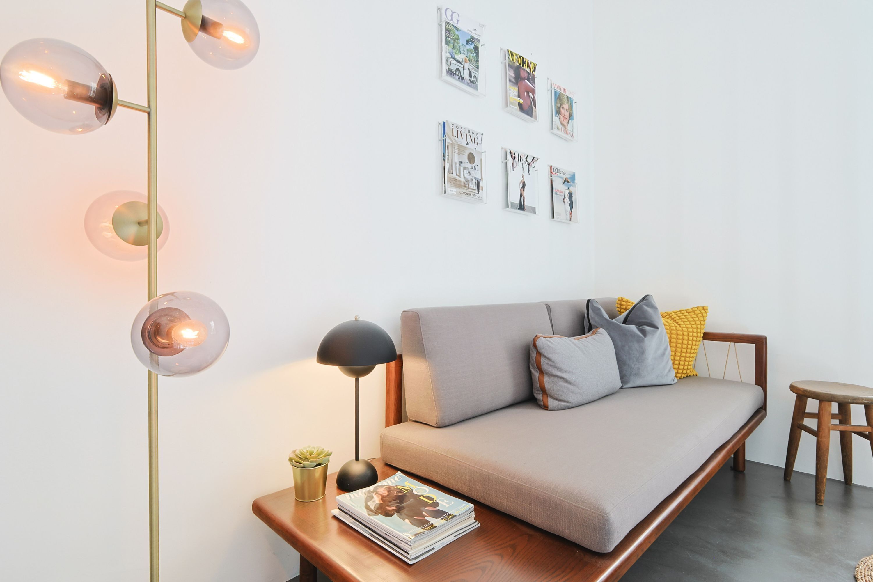 Un salon moderne avec un canapé, une table d’appoint sur laquelle se trouve une lampe, un magazine et un lampadaire à plusieurs ampoules.