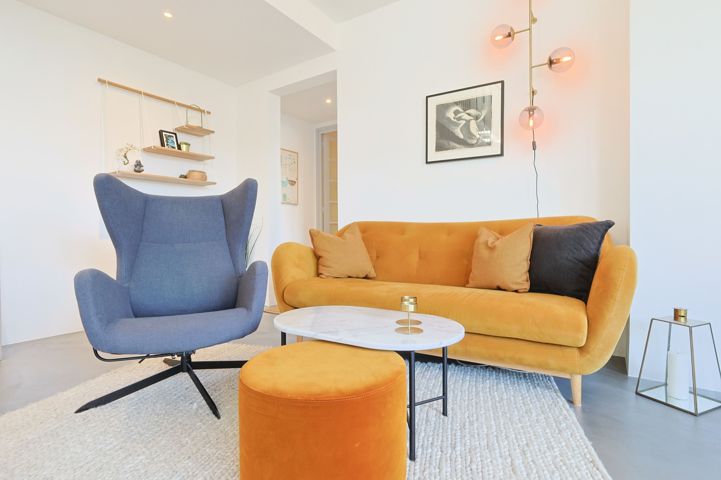 Una sala de estar moderna con un sillón azul, un sofá naranja, una mesita blanca pequeña y una mesita auxiliar de vidrio.