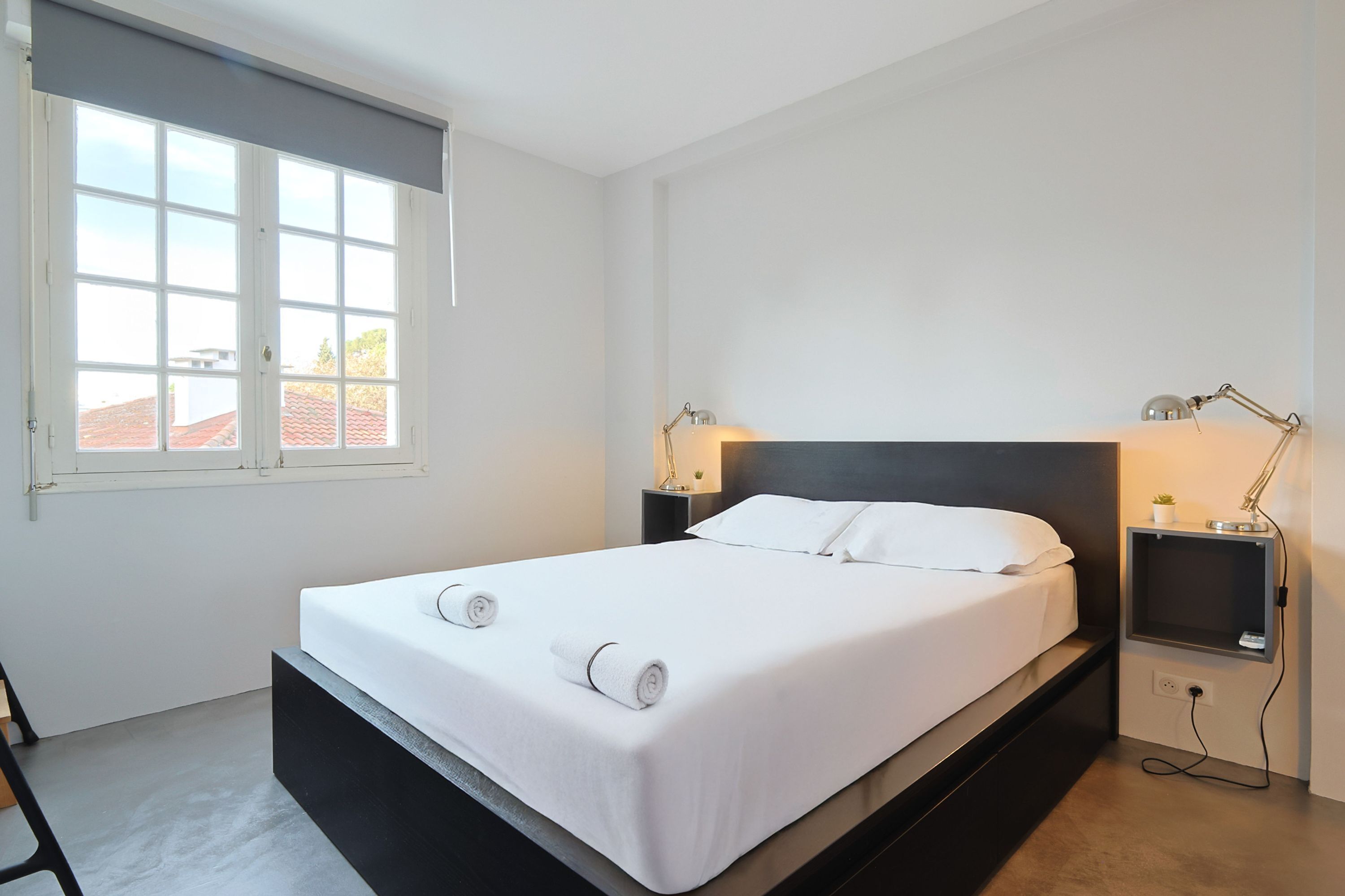 Una habitación de hotel moderna con una cama grande, lámparas de noche, una mesita con una planta y un ventanal con vistas a edificios.