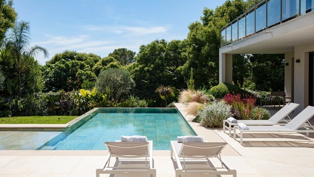 A swimming pool with lounge chairs, surrounded by lush greenery and a modern building. - 004 Villa Le Palm in Le Cannet (Le Cannet)