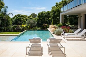 A swimming pool with lounge chairs, surrounded by lush greenery and a modern building. - 004 Villa Le Palm in Le Cannet (Le Cannet)