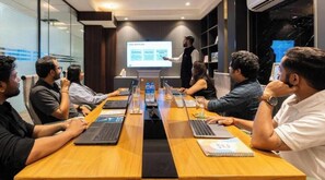 A conference room with a presentation screen, laptops, and attendees seated around a long table. - StayVista Residences near Cyber City Hub (Gurugram)