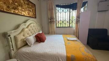 A room with a bed, a round table, a window with curtains, and a painting on the wall.