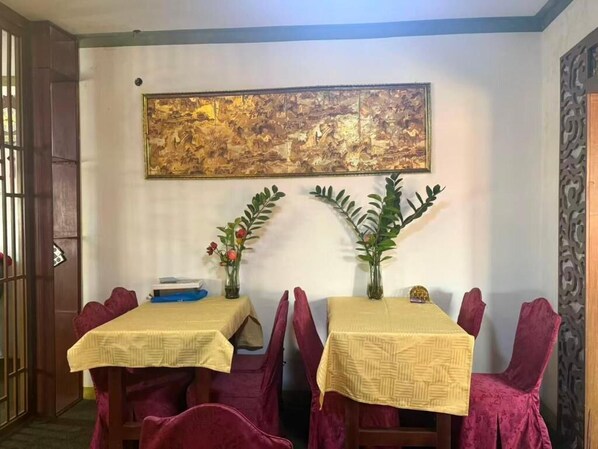 A dining area with two tables, each with a yellow tablecloth and red chairs. There are two vases with flowers on the tables. - Huayun Primier Hotel (Accra)