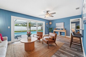 Ein Wohnzimmer mit Blick auf einen Pool, einem Deckenventilator und einem Essbereich mit einem runden Tisch.