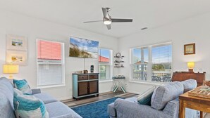 A living room with two sofas, a coffee table, a ceiling fan, and a view through large windows. - Beach House - Coastal Dreaming (Port St. Joe)