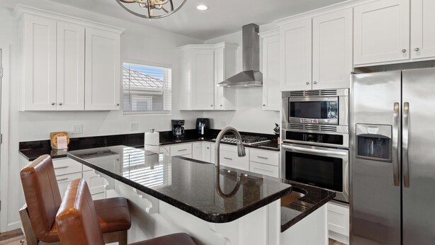 A modern kitchen with white cabinets, a central island, stainless steel appliances, and a chandelier. - Beach House - Coastal Dreaming (Port St. Joe)