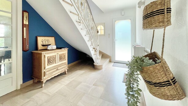Eine Treppe mit aufwendiger Geländergestaltung, ein Holzschrank mit Dekorationsobjekten und hängende Körbe mit Grünpflanzen.