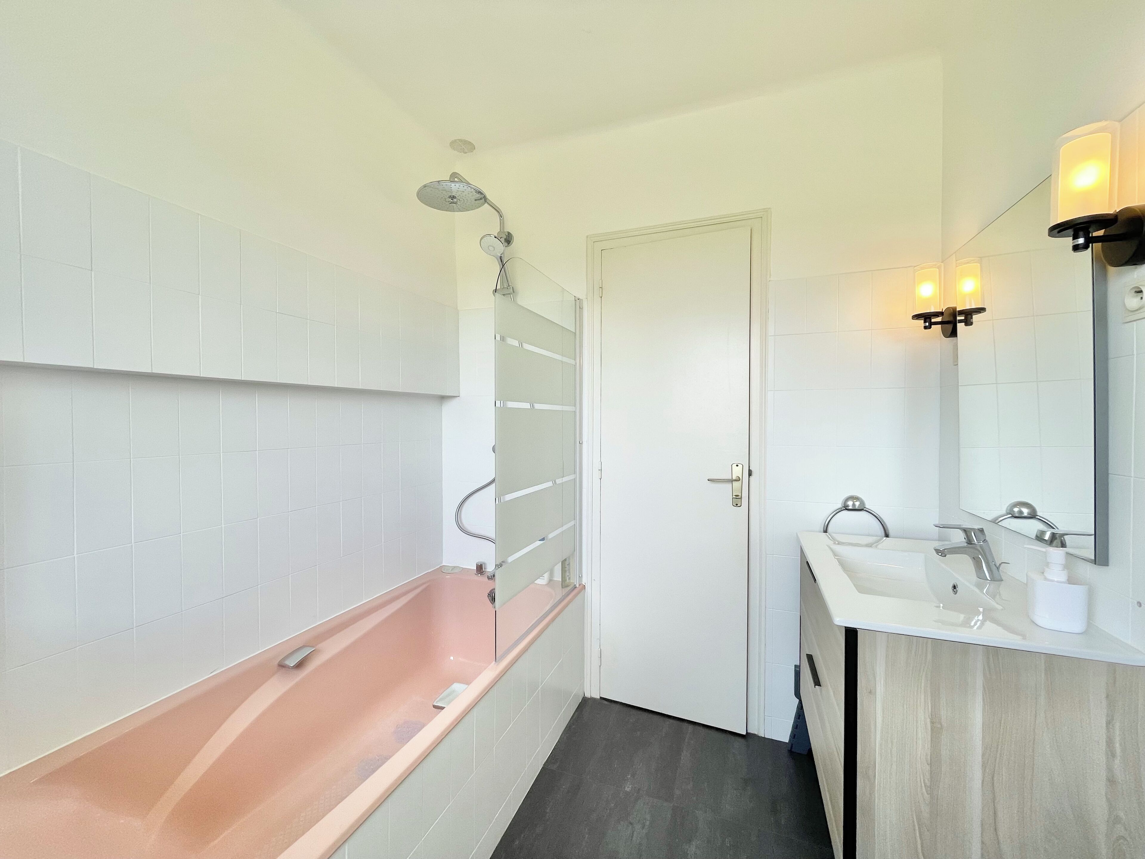 A bathroom with a bathtub, a sink, a mirror, and a door.